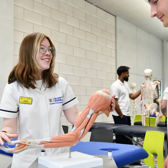 A physiotherapy/sports therapy student demonstrates an anatomical arm model showing muscles and tendons.