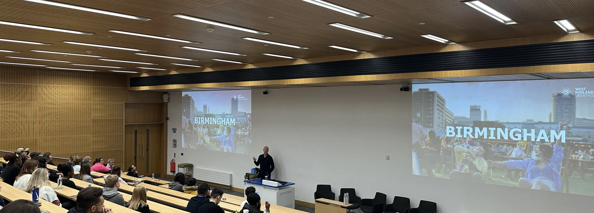 A guest speaker in front of a lecture theatre with word Birmingham on the powerpoint slide
