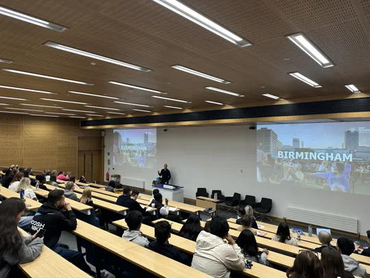 A guest speaker in front of a lecture theatre with word Birmingham on the powerpoint slide