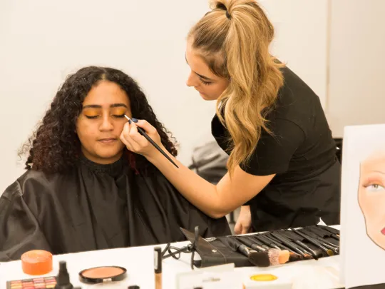 A student applying make-up on a client.