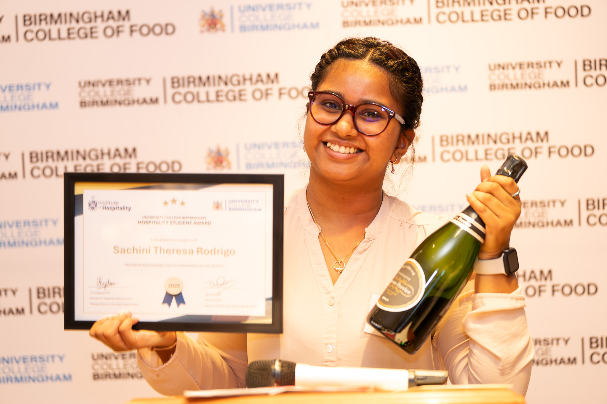 Student smiling with a IoH award and bottle of champagne