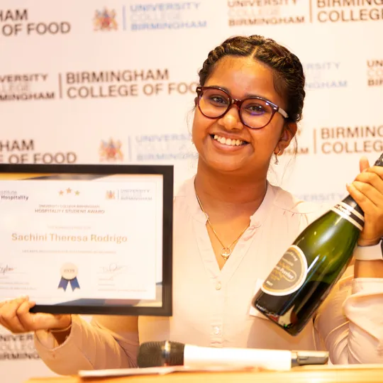 Student smiling with a IoH award and bottle of champagne
