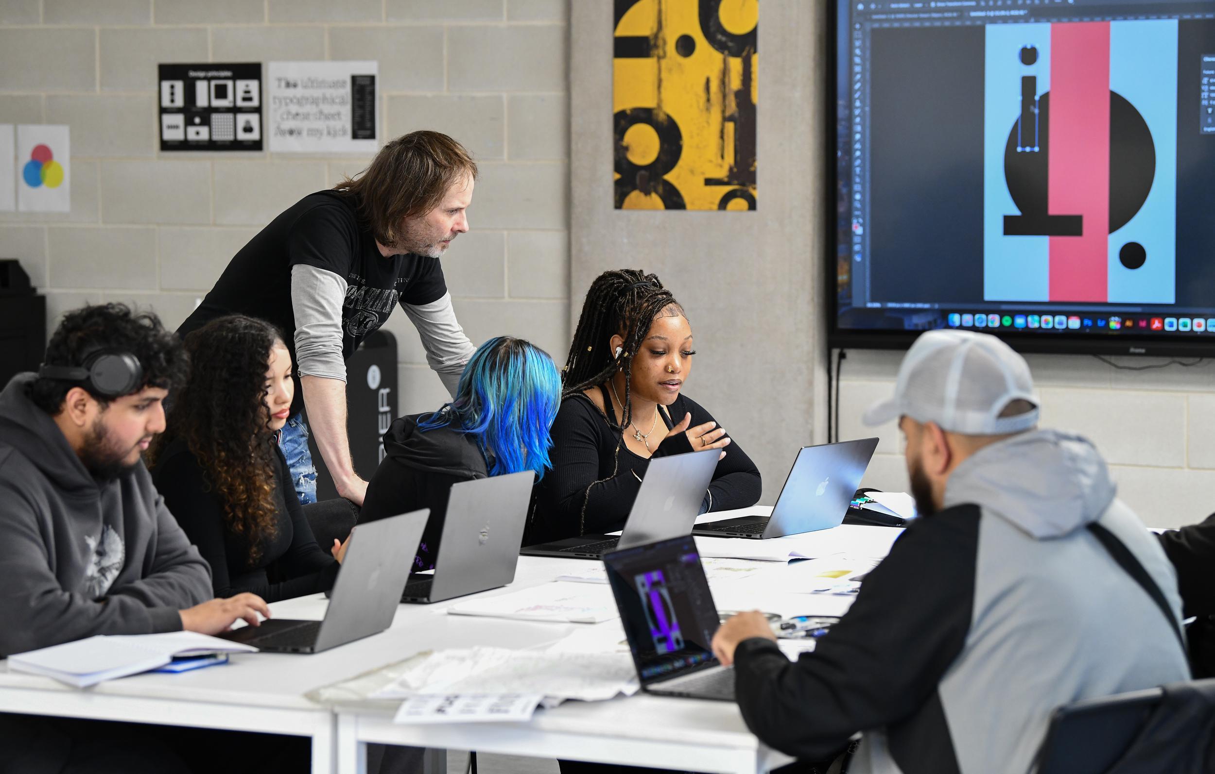 Lecturer and Graphic Design students in a class session working on a project using laptops