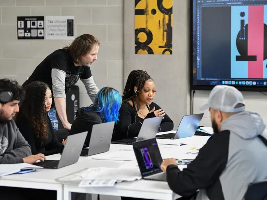 Lecturer and Graphic Design students in a class session working on a project using laptops