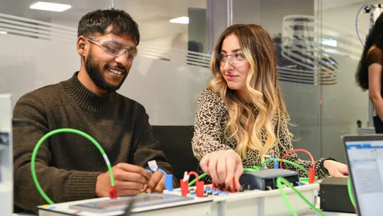 Two student connecting wires on an electric board.