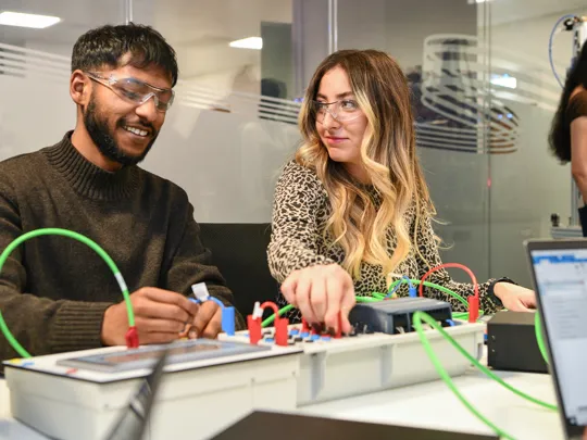 Two student connecting wires on an electric board.