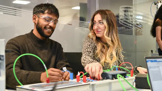 Two student connecting wires on an electric board.