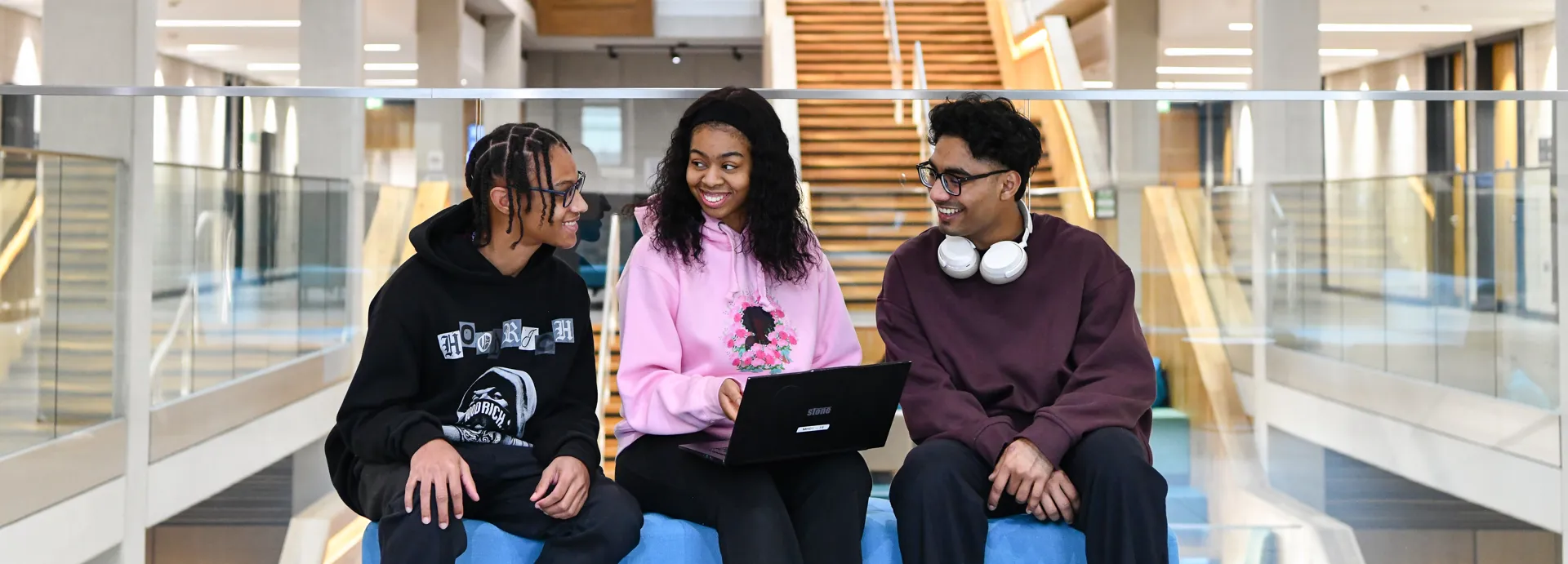 Three students sitting on a blue sofa in Moss House engaging with one another and a laptop on the middle students lap.