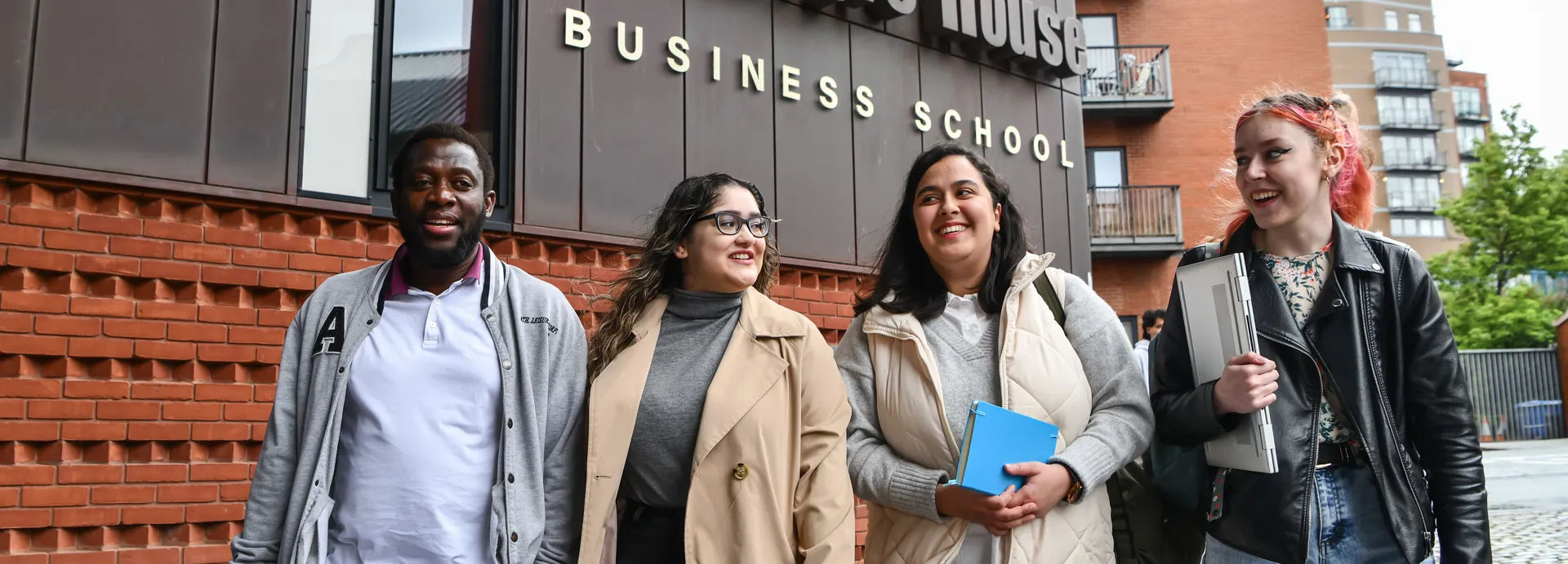 Group of students smiling walking in to campus with a Business school sign above them.