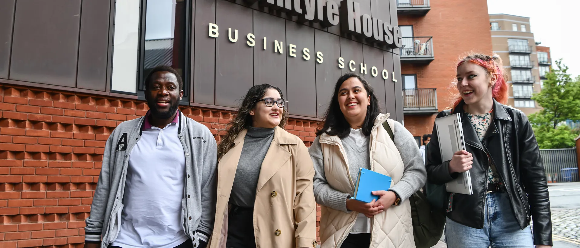 Group of students smiling walking in to campus with a Business school sign above them.