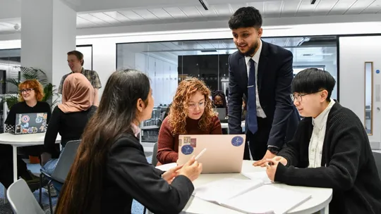Group of young students sat studying together smiling.