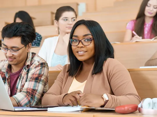 A female student smiling at the camera in a lecture hall with a male student next to her and a female student in the background.