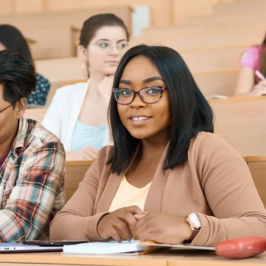 A female student smiling at the camera in a lecture hall with a male student next to her and a female student in the background.