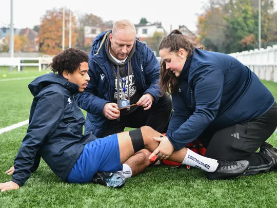 Student and staff member on football field assisting sport injury