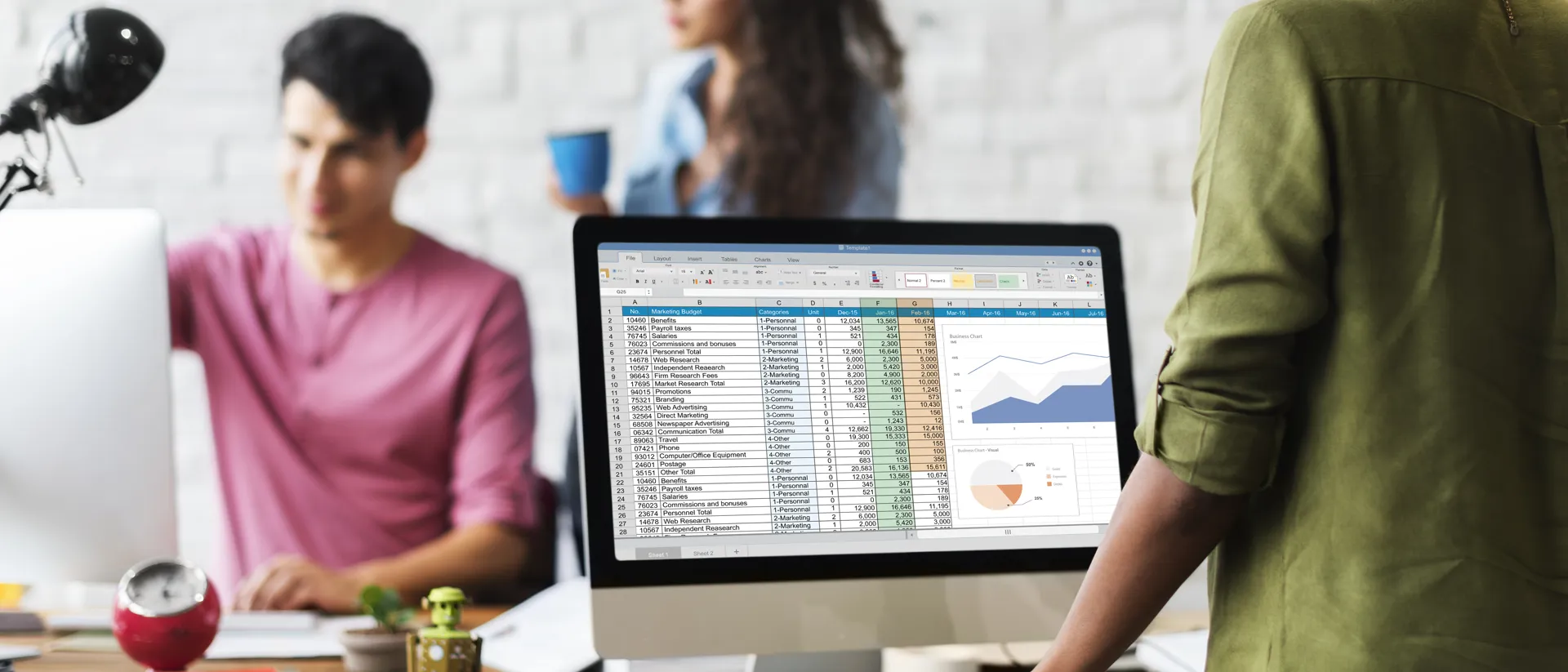 Lady stood in an office environment looking at computer screen with a table and graphs showing.