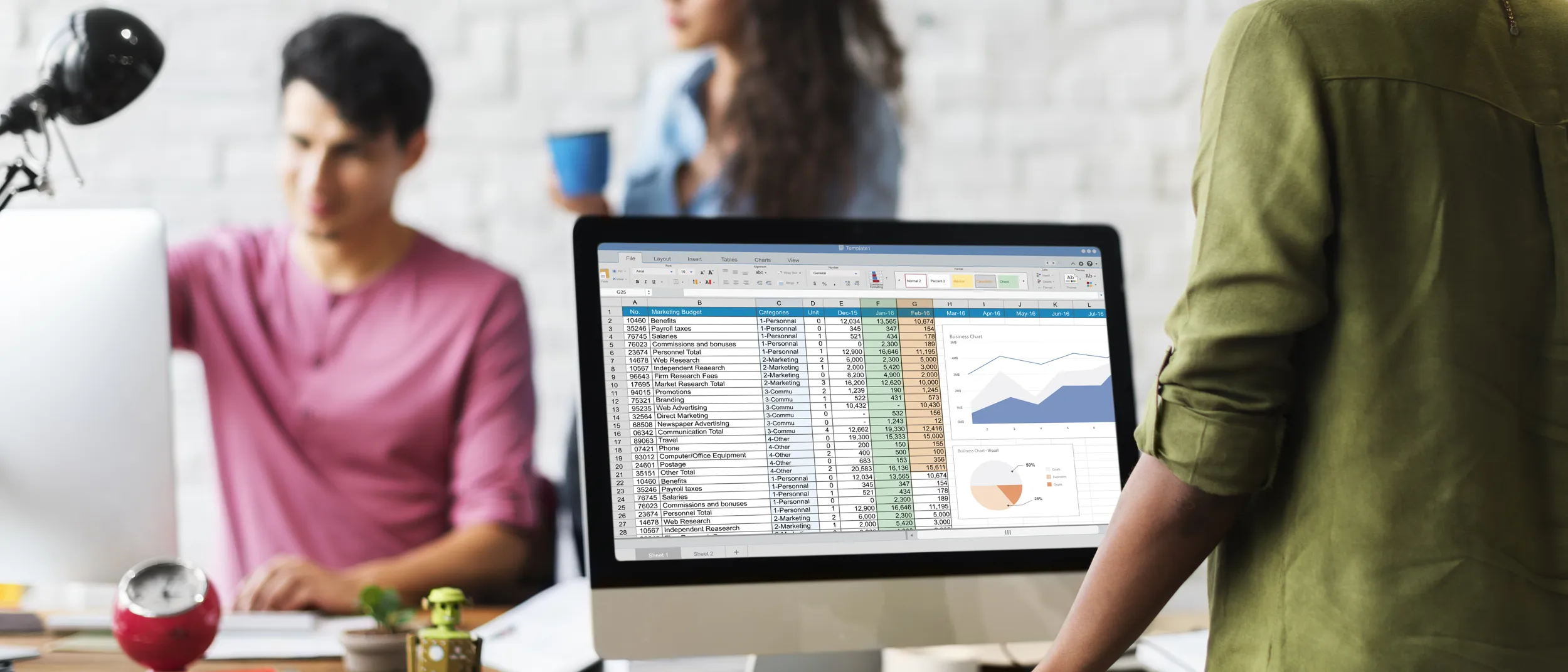 Lady stood in an office environment looking at computer screen with a table and graphs showing.