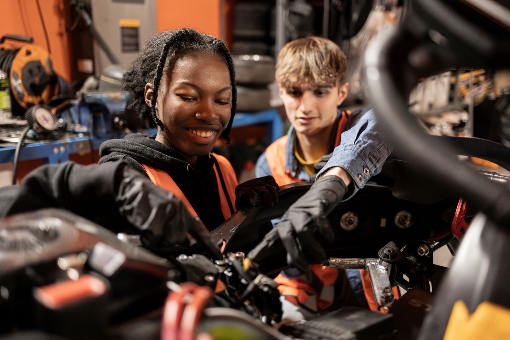 Two young mechanics, one male and one female, working together on engine repairs