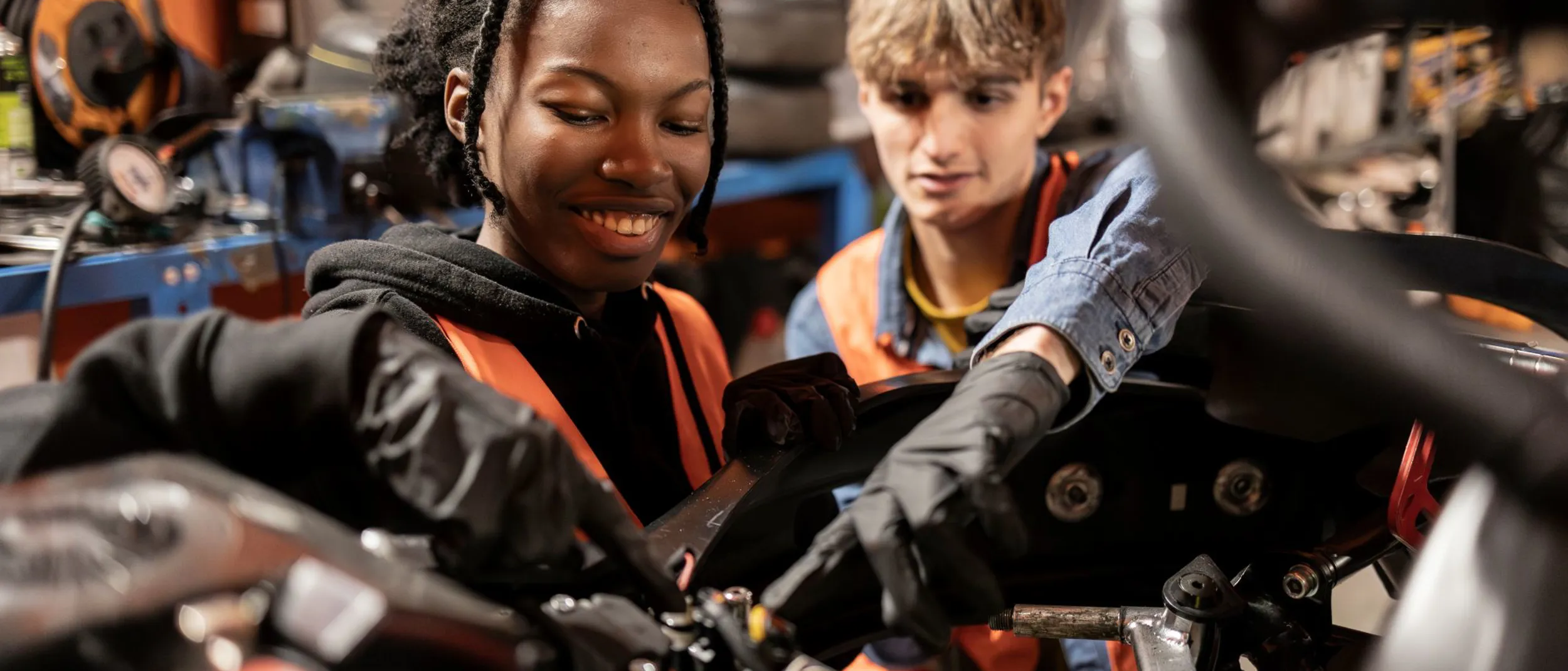 Two young mechanics, one male and one female, working together on engine repairs