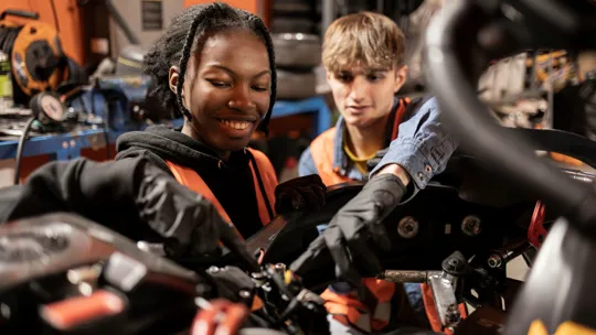 Two young mechanics, one male and one female, working together on engine repairs