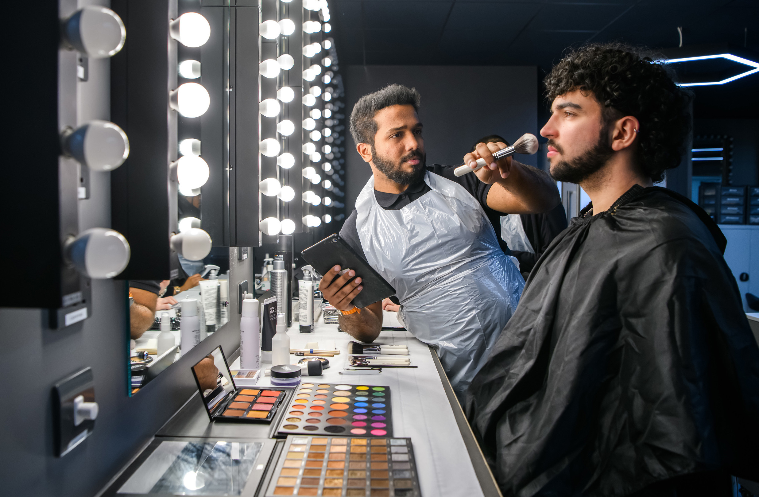 Male student apply make-up to a male model 