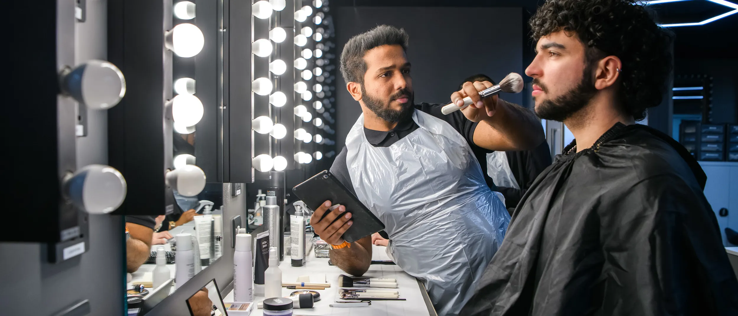 Male student apply make-up to a male model