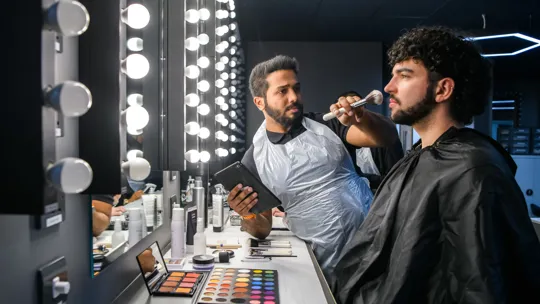 Male student apply make-up to a male model