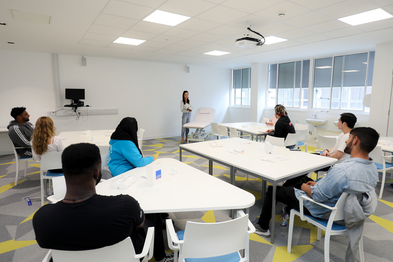 Student in a well light classroom facing forward while a lecturer is presenting.