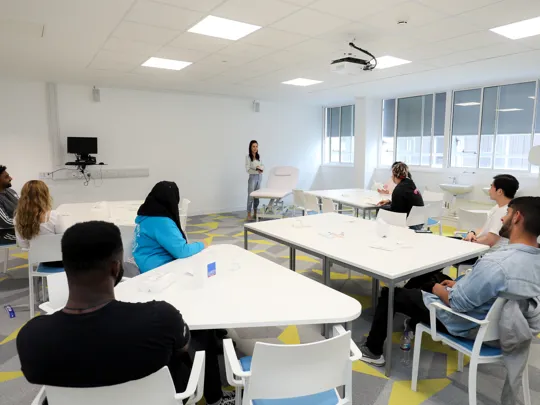 Student in a well light classroom facing forward while a lecturer is presenting.