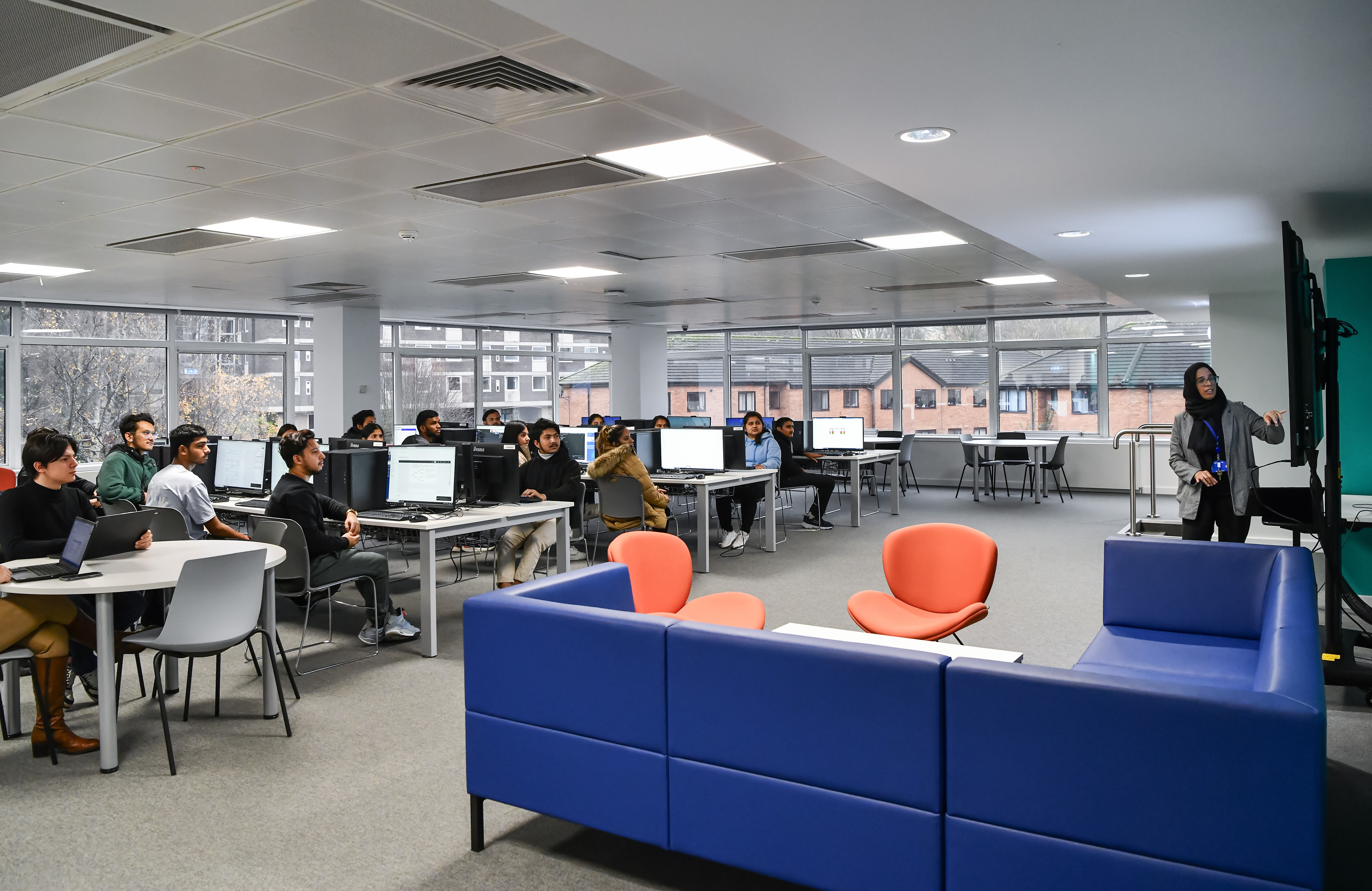 Computer classroom filled with students being taught by a female lecturer.