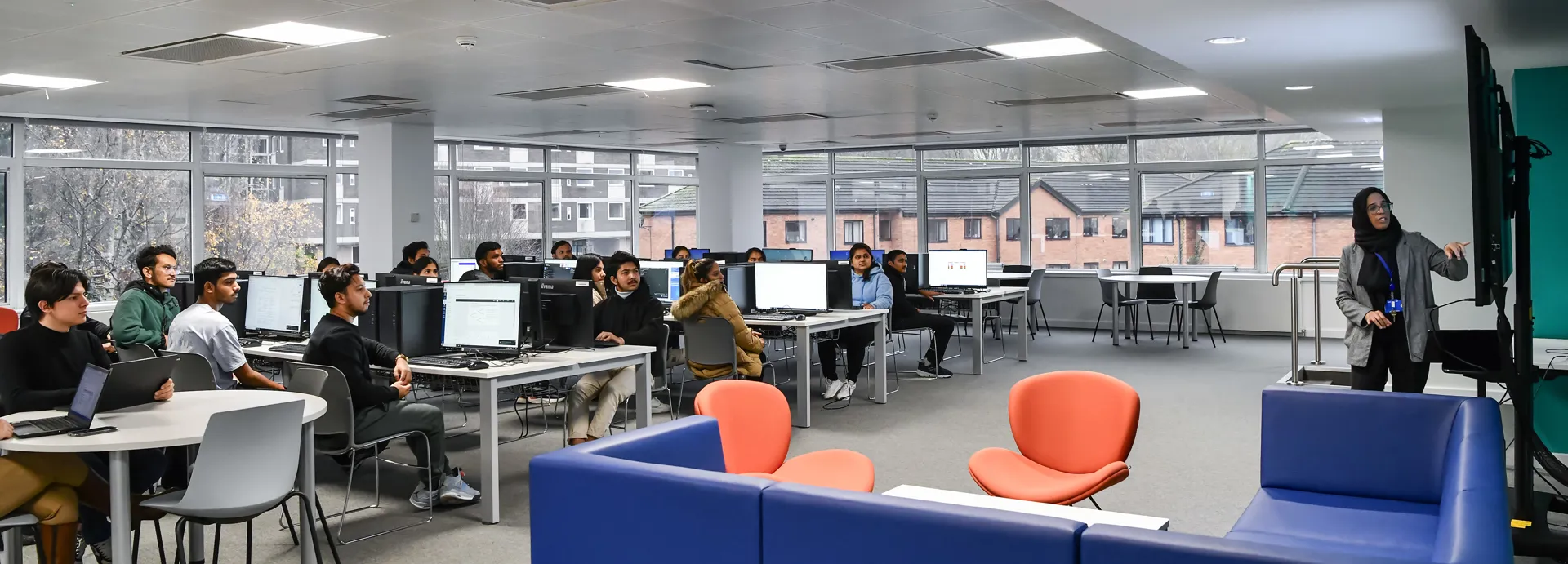 Computer classroom filled with students being taught by a female lecturer.