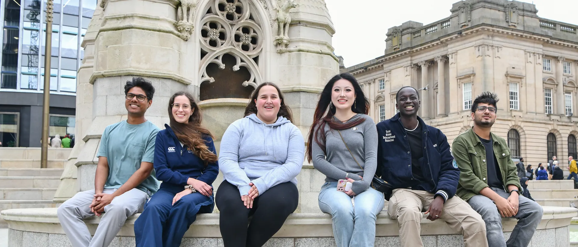 A diverse group of students sat on a fountain smiling.