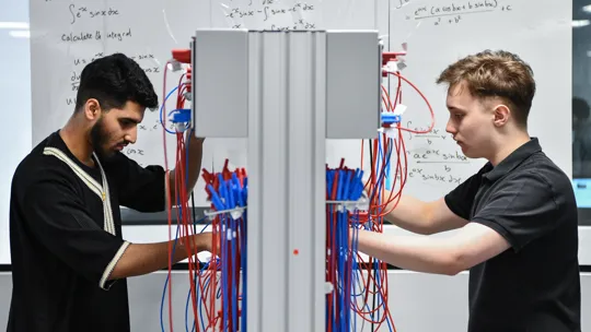 Two male student wiring up a board.