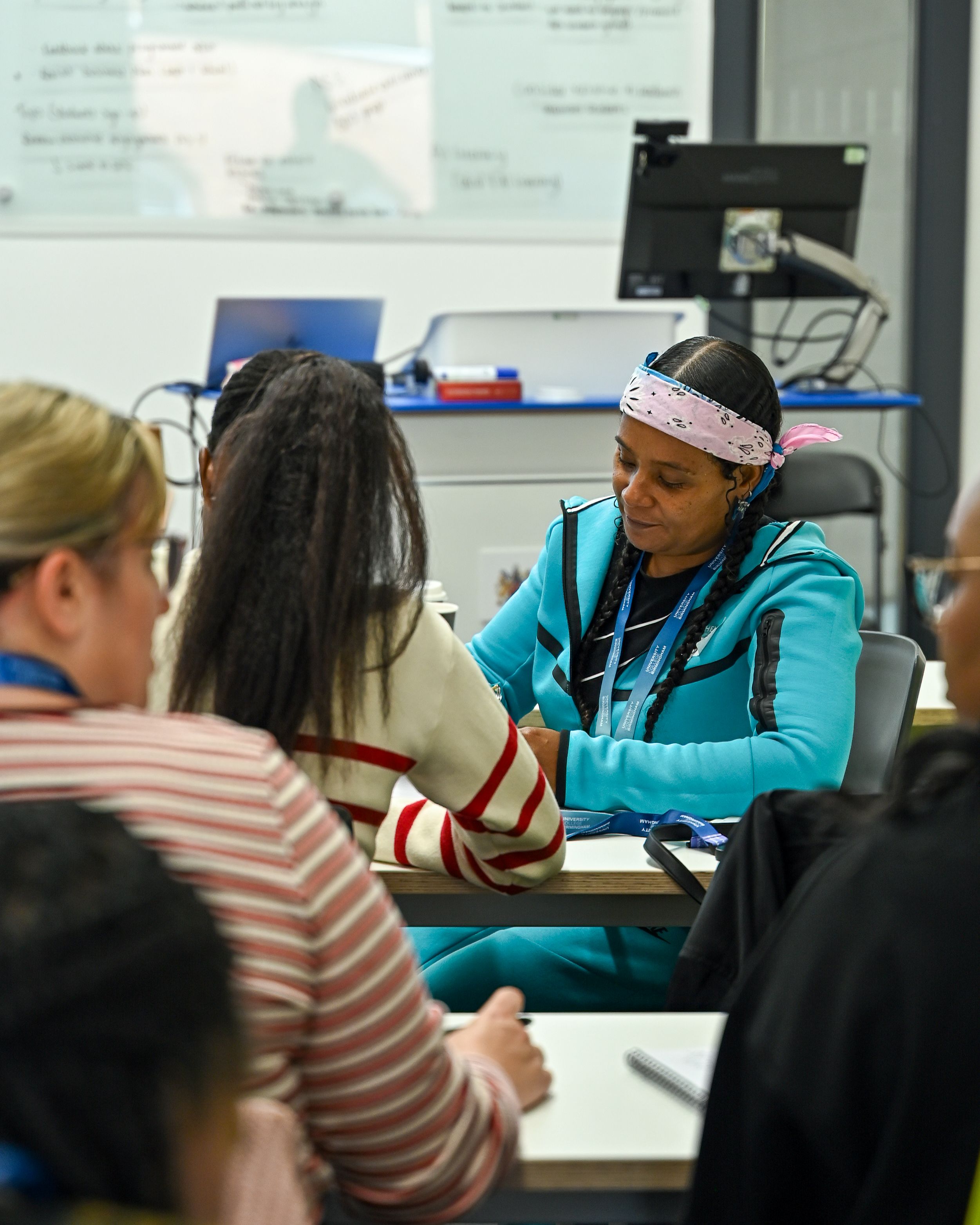 A student sits looking down at her work, she wears a bright blue tracksuit and a bandanna. She is one of the new students on UCB's social apprenticeship courses.