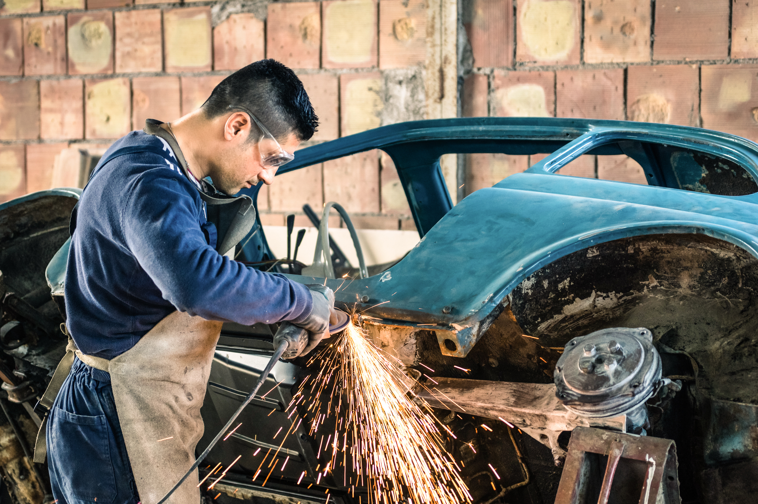 Young man mechanical worker repairing an old vintage car body in a garage