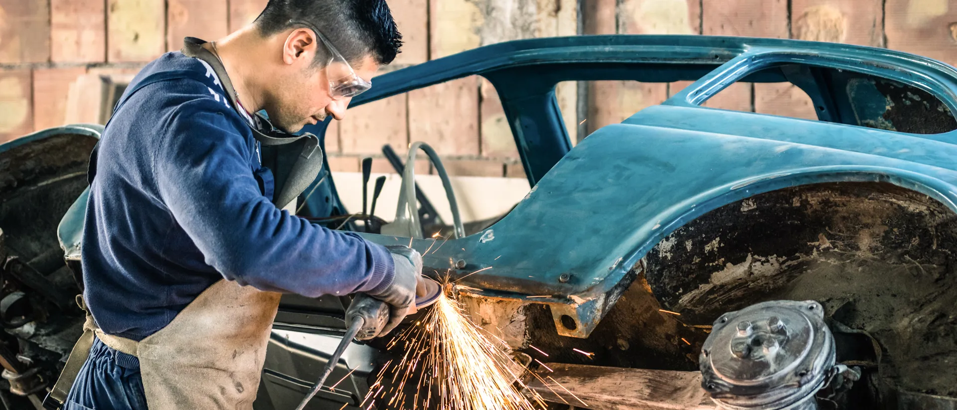 Young man mechanical worker repairing an old vintage car body in a garage