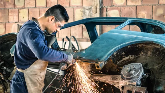 Young man mechanical worker repairing an old vintage car body in a garage