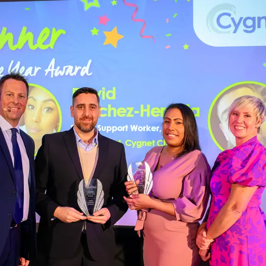 Four people standing infront of a projector at the Cygnet Awards show smiling after being nominated for awards.