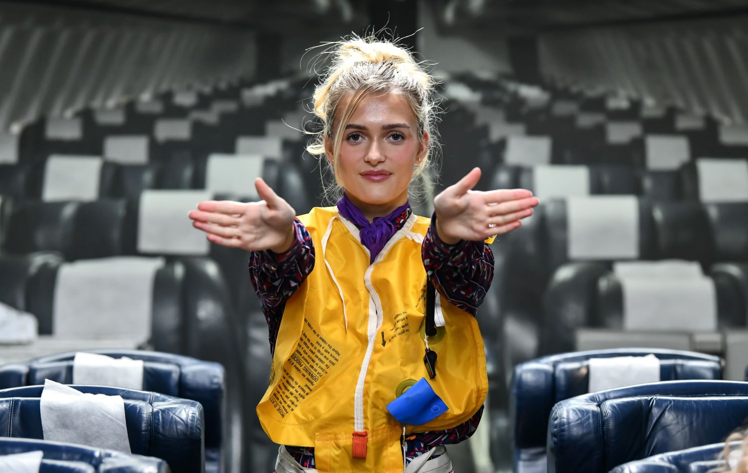 Female student in a mock airplane with life vest pointing to exits.