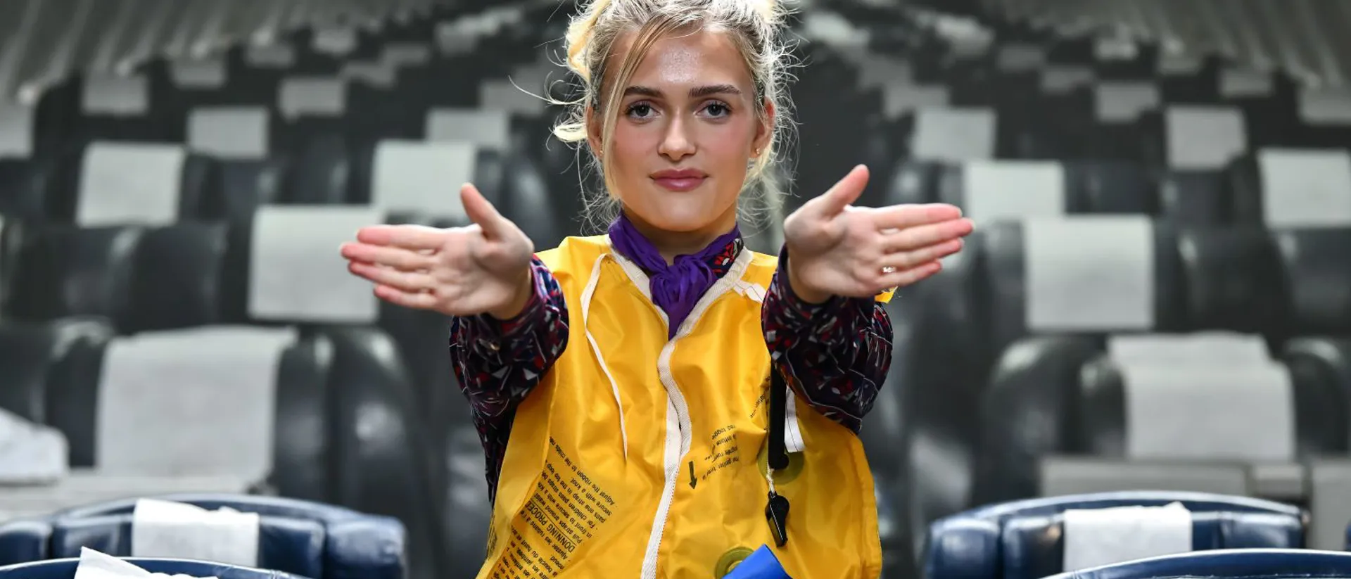 Female student in a mock airplane with life vest pointing to exits.