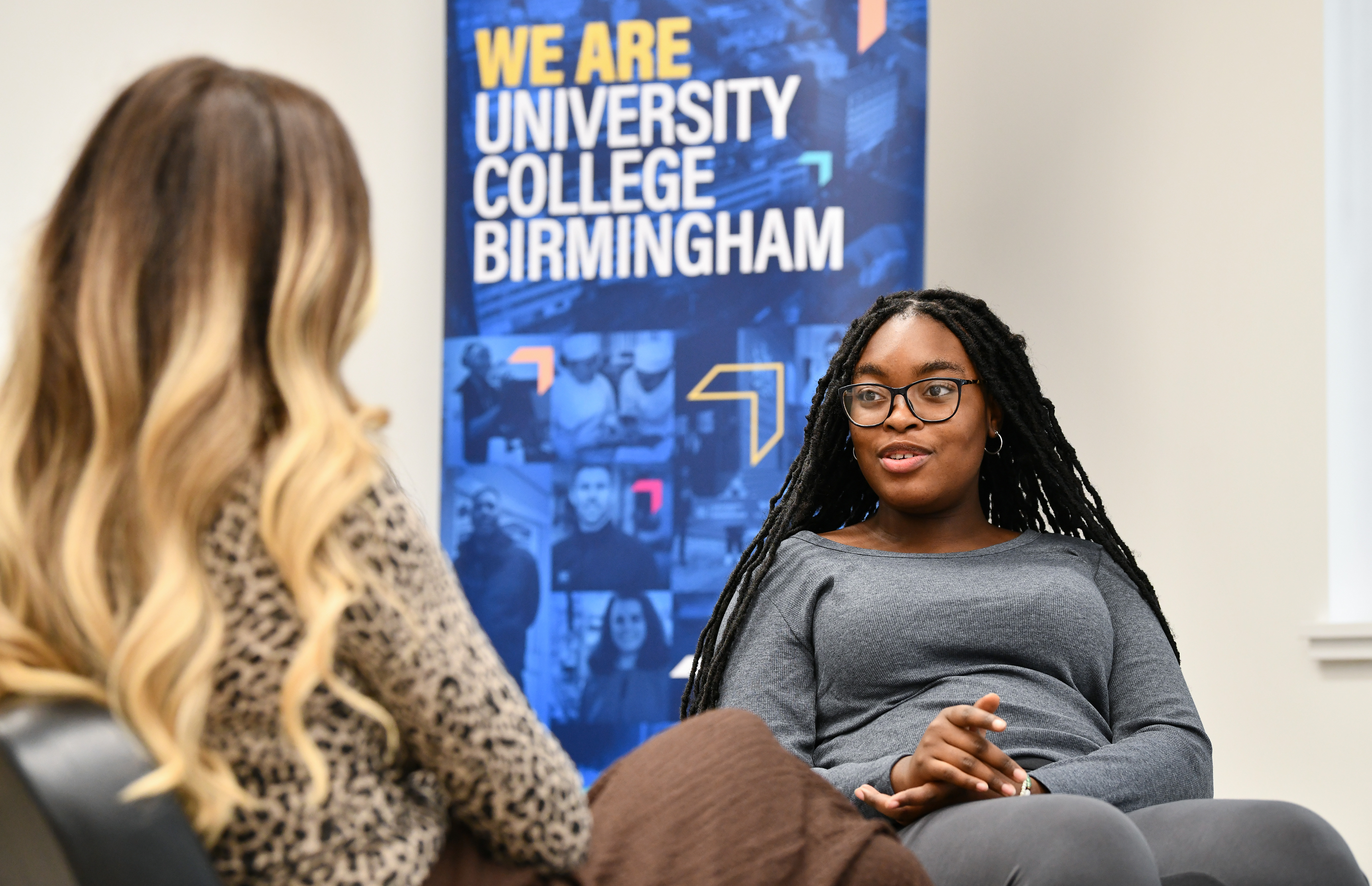 Two students sat talking with a banner that says we are University College Birmingham behind them.