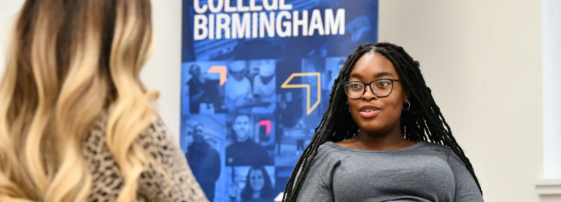 Two students sat talking with a banner that says we are University College Birmingham behind them.