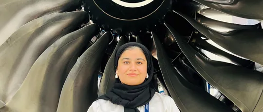 Female student sat in front of a airplane turbine.