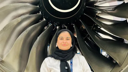 Female student sat in front of a airplane turbine.