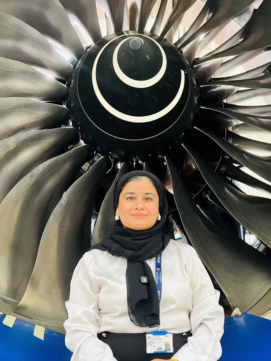 Female student sat in front of a airplane turbine.